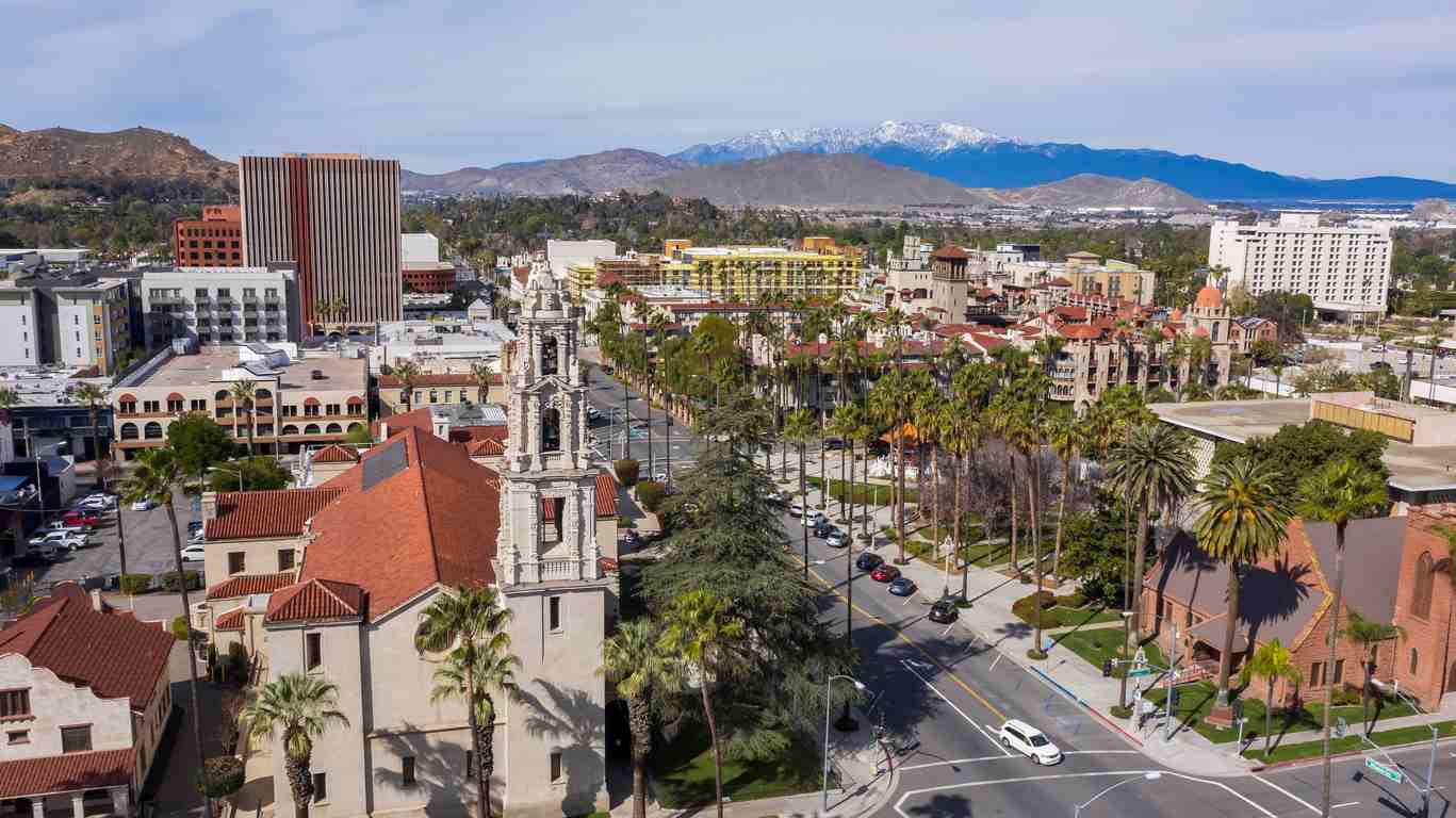 An aerial view of Riverside, CA featuring a popular street, palm trees, and mountains. 