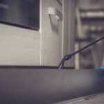 A person wearing blue gloves uses a spray wand to apply effective pest control solutions along the base of kitchen cabinets, targeting ants.